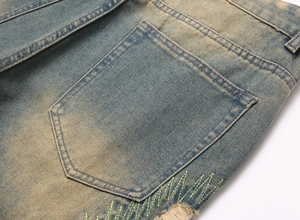Macro view of vintage washed denim pocket with green Z-shaped embroidery and distressed edge