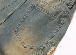 Macro shot of green wavy embroidery and distressed fraying on vintage wash denim jeans