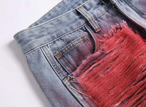 Detail of light blue denim pants featuring red fringe tassels and metal rivet accents