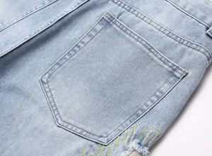 Detailed close-up of light blue denim pocket with yellow embroidery and frayed edges