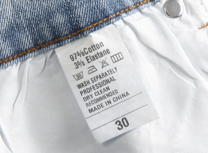 Macro detail of the product care label showing 97% cotton fabric and size 30 on denim pants