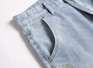 Detail of light blue washed denim waist with yellow sun embroidery and metal rivets