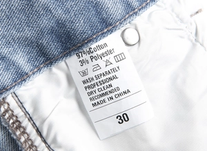Macro shot of garment care label on high street distressed denim jeans showing material specs