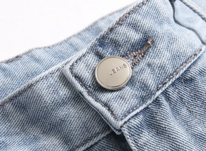 Detailed close-up of blue denim jeans waist with silver button and JEANS engraving