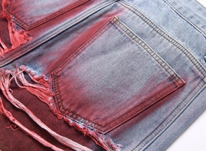 Detail view of light blue denim jeans featuring vibrant pink spray paint and heavy distressing