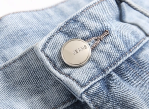 Close-up of engraved metal button and waist detail on light blue distressed denim jeans