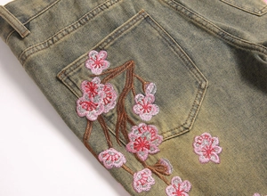 Macro detail of plum blossom embroidery on retro yellow-washed denim jeans pocket