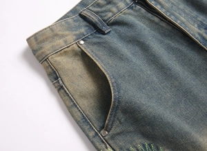 Macro detail of vintage washed denim jeans featuring green embroidery and metal rivets