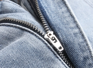 Detailed macro shot of the metal zipper fly and stitching on blue denim jeans