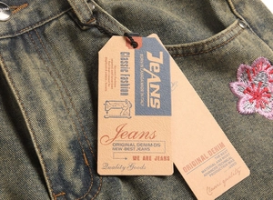 Detail of vintage washed denim jeans with pink cherry blossom embroidery and brand tags