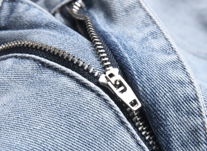 Detailed close-up of heavy-duty metal zipper and denim twill texture on high-street jeans