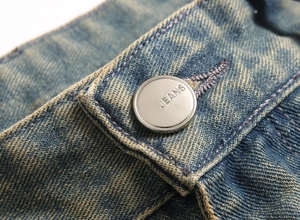 Detail of vintage blue denim jeans featuring a silver metal button with JEANS engraving