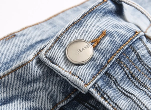 Macro shot of silver button with Jeans text on light blue washed slim flare denim jeans