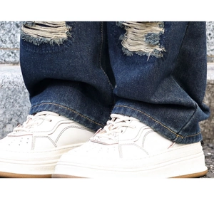 Gros plan sur un jean droit déchiré pour homme avec des baskets blanches à semelles épaisses