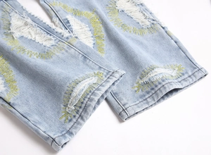 Detail of distressed light blue denim jeans with yellow star embroidery and frayed edges