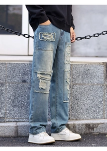 Detail of distressed light blue denim jeans with vintage patchwork and frayed edges