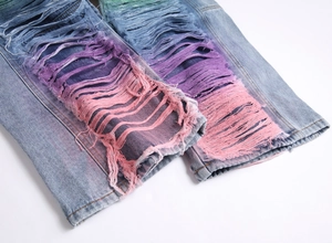 Detail view of light blue jeans with rainbow gradient dyeing and distressed ripped holes