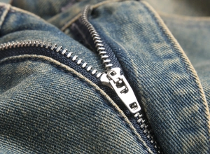 Macro shot of silver metal zipper and blue denim texture on vintage distressed jeans