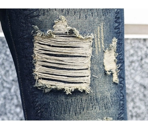 Détail de jean bleu usé avec déchirures marquées et coutures de renfort décoratives