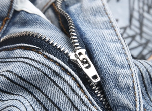 Macro shot of durable metal zipper and distressed thread details on light blue denim jeans