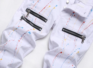 Detail of white slim-fit jeans featuring colorful paint splatter and metal zippers