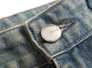 Macro shot of silver metal button and waist detail on distressed blue denim jeans