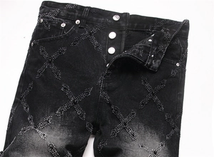 Close-up of black washed denim jeans with distressed cross patches and bead details