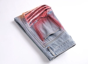 Detail of light blue denim pants with red spray paint effect and distressed frayed pockets