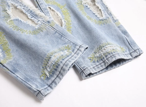 Detail of light blue distressed jeans featuring yellow sunburst embroidery on the hem