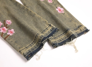 Detail of vintage washed green denim with pink cherry blossom embroidery and frayed hem