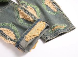 Detailed close-up of distressed denim hem with green zigzag stitching and frayed edges