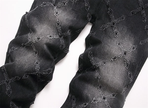 Detail of black washed denim jeans featuring cross patches with shiny black bead accents