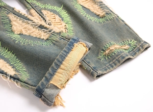 Close-up of distressed denim jeans with neon green embroidery and frayed ripped edges