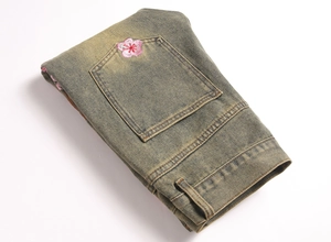 Detailed close-up of pink cherry blossom embroidery on vintage acid-wash denim jeans