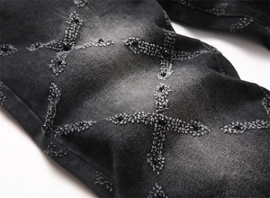 Detail of distressed grey denim jeans with punk style cross patches and black pearl beads