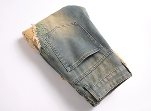 Detailed view of vintage distressed denim pants with green contrast stitching and frayed edges