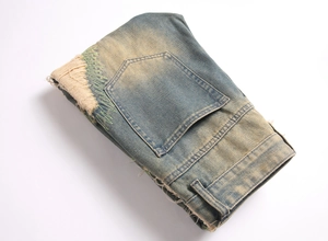 Detail of vintage blue distressed jeans featuring yellow wash effect and green embroidery