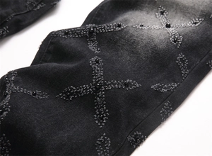 Close-up of black denim fabric with cross stitching and bead detail on jeans