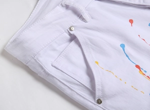Detailed close-up of white slim fit jeans featuring metal rivets and colorful paint splatter