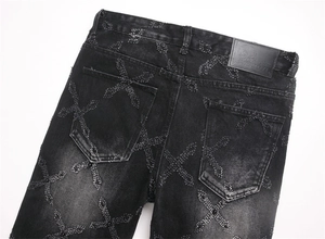 Detail of cross-shaped frayed embroidery and leather patch on black punk denim jeans