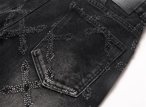 Detailed close-up of raw-edge cross patterns on a black washed denim pocket