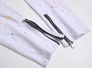 Detail view of white stretch jeans featuring colorful paint splatters and ankle zipper hem