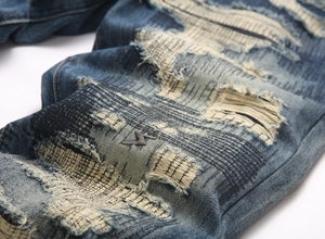 Detail of distressed dark blue jeans featuring complex patch repairs and lightning embroidery