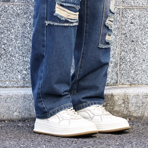Distressed ripped blue denim pants styled with platform white sneakers on urban pavement