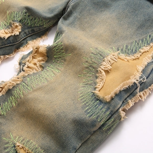 Vintage washed blue denim jeans with distressed holes and green zigzag embroidery