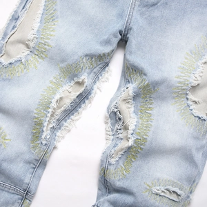 Distressed light blue denim jeans featuring yellow starburst embroidery around torn holes
