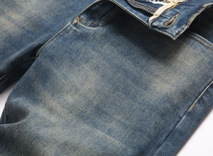 Detail view of mid-blue denim fabric with washed effect, metal zipper, and reinforced stitching