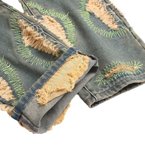 Distressed American vintage blue jeans with ripped holes and neon green embroidery detail