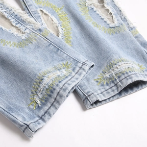Distressed light blue denim jeans featuring yellow sunburst embroidery and ripped details