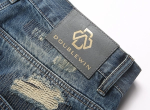 Detail of blue distressed denim jeans showing textured fabric and golden logo leather patch